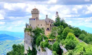 San Marino: en medeltida borg tronar på en klippavsats, omgiven av grönskande träd och med en vidsträckt vy över kullar och berg.