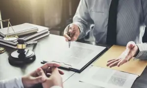 Dwóch mężczyzn przy biurku z dokumentami, młotkiem sędziowskim i wagą sprawiedliwości.