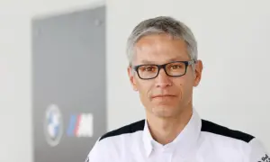 Mike Krack, con gafas y camisa blanca con detalles negros, posa frente a un logo de BMW M.