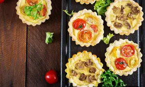 Mini quiches apéro aux tomates et champignons, garnies de feuilles de salade verte, sur fond de bois sombre.