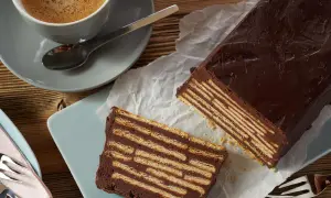 Schokoladiger kalter Hund, geschichtet mit Keksen, neben einer Tasse Kaffee.