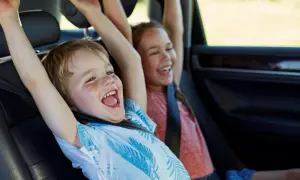 Niños emocionados en el coche, con los brazos en alto. Parecen haber alcanzado la altura mínima para no usar silla en el coche.