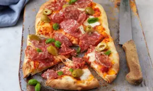 En härlig zeta pinsa med salami, oliver och färsk basilika, redo att avnjutas.
