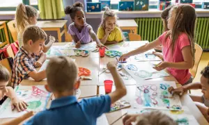 Niños y niñas disfrutan del arte en infantil, pintando con acuarelas y pinceles en una clase creativa.