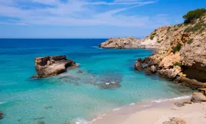 Aguas cristalinas y rocas escarpadas en una cala idílica. Unos pequeños **planes** se ven en el horizonte, invitando a soñar con esta **playa** paradisíaca.