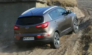 Brązowy Kia Sportage 2014 zjeżdża po piaszczystej ścieżce, unosząc kurz.