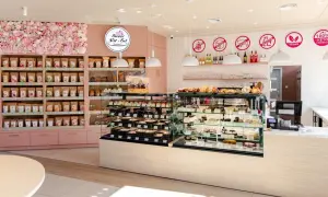 Wnętrze cukierni "Sweet Fit & Eat" z witrynami pełnymi ciast i ciasteczek. Reklama cukierni podkreśla opcje bez glutenu, cukru i laktozy.