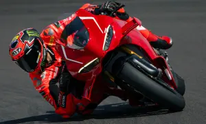 Motocyklista w czerwonym kombinezonie pochyla się na torze na swoim czerwonym Ducati Panigale V4.
