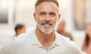 Uśmiechnięty mężczyzna w średnim wieku z siwą brodą i niebieskimi oczami, ubrany w jasną koszulkę polo.