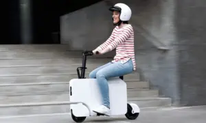 Uśmiechnięta kobieta w kasku jedzie na białym Honda Motocompacto, pokonując miejskie schody.