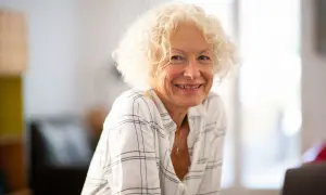 Une femme souriante aux cheveux bouclés blonds, portant une chemise à carreaux. Son état civil célibataire rayonne de joie.