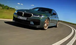 Zielony BMW M5 CS na zakręcie drogi, z rozmytym tłem i niebieskim niebem.