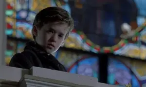 Chłopiec z filmu "Szósty zmysł" Haley Joel Osment w kościele, za nim witraż.