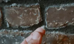 Ein Finger berührt weiße Ablagerungen auf einer Ziegelwand. Dies zeigt, wie Salpeter entsteht, oft durch Feuchtigkeit und chemische Reaktionen.