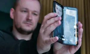 Mężczyzna trzymający składany smartfon, na ekranie którego widać jego twarz.
