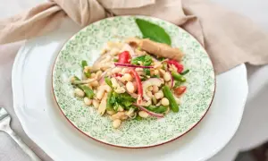 Ein bunter Thunfisch-Bohnen-Salat, italienisch inspiriert, mit grünen Bohnen, roten Zwiebeln und Tomaten auf einem Teller mit grünem Muster.