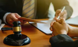 Sędzia z młotkiem i dokumentami, prawnik pisze, klient z modlącymi się dłońmi. Rozważana sankcja kredytu darmowego.