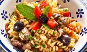 Fusilli con pesce spada, pomodorini, olive nere e menta fresca in una ciotola decorata.