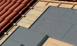 Dettaglio di un tetto con tegole rosse, tavolato in legno e pannelli grigi per l'isolamento tetto esistente.