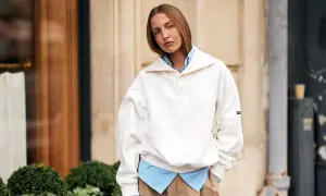 Frau kombiniert lässig ein gestreiftes Hemd mit einem weißen Pullover, der wie ein Hoodie wirkt.