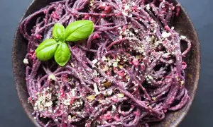 Fioletowy makaron z pesto z buraków, posypany orzechami i udekorowany listkami bazylii.