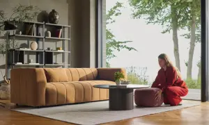 En kvinna i rött sitter på en puff framför en soffa i en miljö som utstrålar dansk inredningsstil.