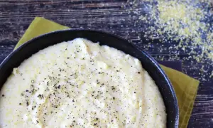 Kremowa polenta w czarnej patelni, posypana świeżo mielonym pieprzem, na drewnianym tle.