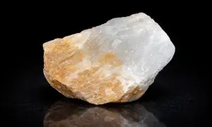 Ein unregelmäßiger, weiß-gelblicher alabaster stein mit glatter Oberfläche und reflektierender Unterseite auf schwarzem Hintergrund.