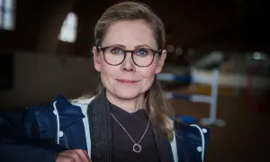 Anna Schreil med glasögon och en blå jacka, står i en ridhall.