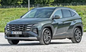 Nowy, tani SUV Hyundai Tucson w ciemnozielonym kolorze, zaparkowany na żwirowej drodze.