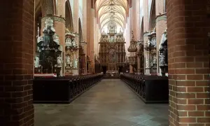 Wnętrze katedry w Pelplinie z rzędami ławek i bogato zdobionym ołtarzem głównym.
