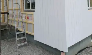 Byggarbetsplats där man valt att kombinera liggande och stående panel på husfasaden. En stege står redo.