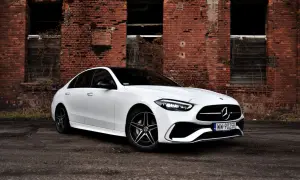 Biały Mercedes 220 z czarnym dachem zaparkowany przed zniszczoną ceglaną ścianą.