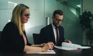 Kobieta i mężczyzna w okularach siedzą przy biurku i przeglądają dokumenty.