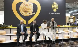Män sitter på stolar framför en stor vägg med en bild av pasta och texten "GRANA PADANO. Un'emozione italiana.