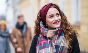 Uśmiechnięta dziewczyna w bordowej opasce i kolorowym szalu, idealnym do płaszcza w kratę. W tle para spacerująca ulicą.