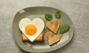 Jajko sadzone w kształcie serca na grzance, obok tostów w kształcie serc i liści szpinaku.
