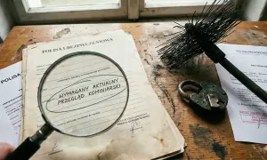 Pod lupą dokument "Wymagany aktualny przegląd kominiarski" obok szczotki kominiarskiej i kłódki. Wartość rzeczywista a odtworzeniowa w kontekście ubezpieczenia.