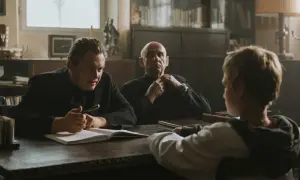Trzech mężczyzn przy stole, jeden z nich pisze. Scena z filmów Piotra Domalewskiego.