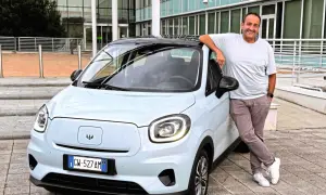 Uśmiechnięty mężczyzna opiera się o jasny samochód elektryczny Leapmotor T03.