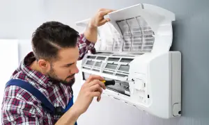 Technik z wkrętarką naprawia otwartą jednostkę klimatyzacyjną zamontowaną na ścianie.