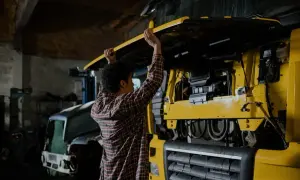 Un mécanicien examine les différentes parties d'un camion jaune, soulevant le capot pour accéder au moteur.