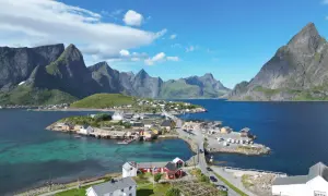 Idyllisches Dorf an der Küste mit roten und weißen Häusern, umgeben von majestätischen Bergen. Tolle Lofoten Tipps für Ihren Urlaub!