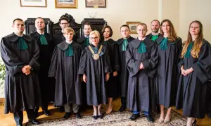 Grupa prawników w togach stoi w pomieszczeniu z meblami i obrazami.