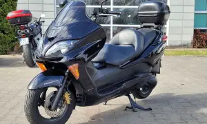 Czarny skuter Honda Forza 250 z kufrem na bagaż, zaparkowany przed budynkiem.