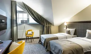 Pokój hotelowy z dwoma łóżkami, żółtym fotelem i biurkiem. Idealne miejsce na nocleg, gdzie gwiazdki w hotelach są gwarancją komfortu.