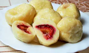 Pyszne, domowe knedle ze śliwkami, posypane cukrem, na białym talerzu. Jedna połówka ukazuje soczyste, czerwone wnętrze.