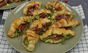 Słone rogaliki z ciasta francuskiego z szynką parmeńską i rukolą, podane na talerzu.