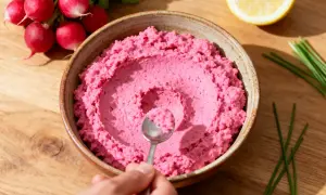 Un bol de tarama maison rose vif, garni de radis, d'une tranche de citron et de ciboule.