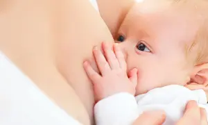 Ein Baby trinkt an der Brust. Die Hand des Babys ruht auf der Brust, was die Milchproduktion anregen kann.
